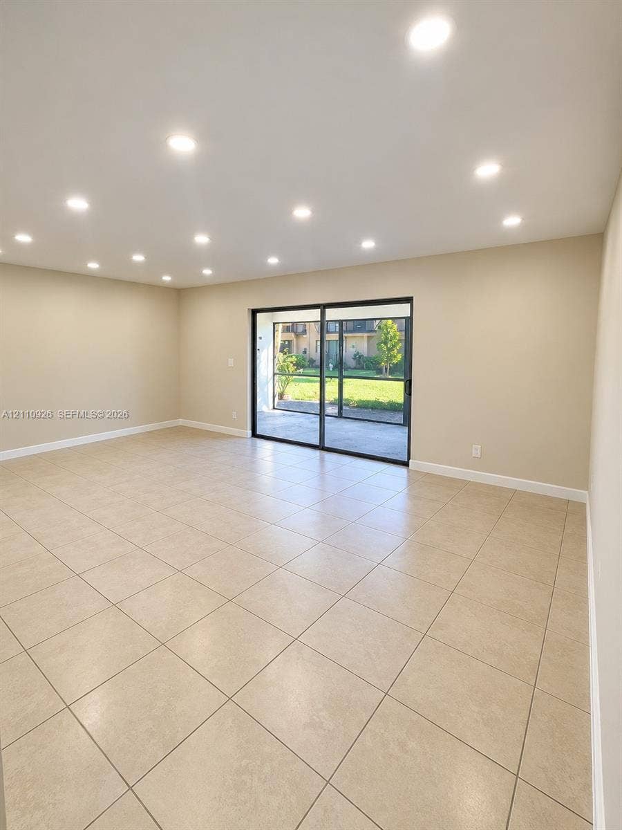 Neutral-toned room featuring large-format tile flooring, recessed ceiling lighting, and sliding glass doors with black framing