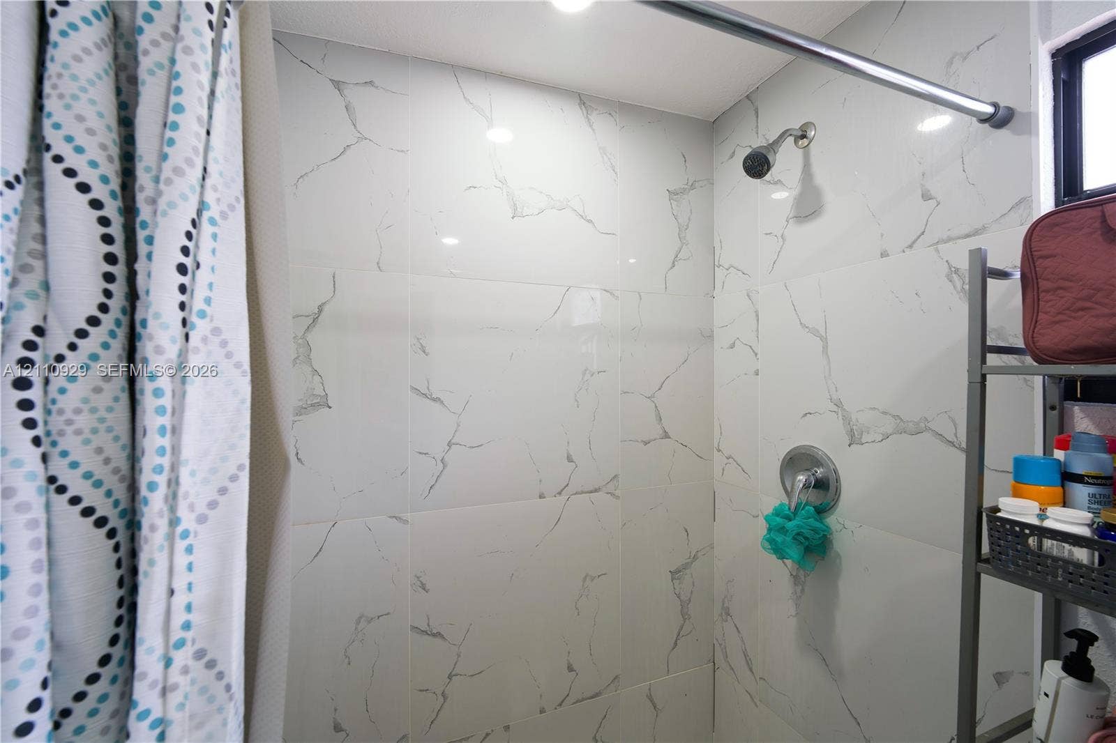 Shower stall featuring large-format white stone-finish wall tiling with grey veining, a chrome fixed shower head, and a chrome single-handle pressure balance valve