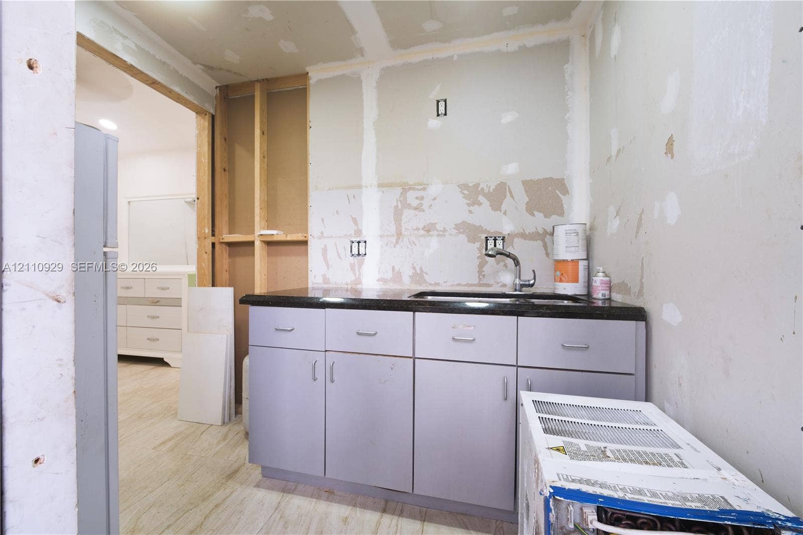 Kitchen area featuring grey cabinetry, dark stone-finish countertop, and stainless steel sink with faucet
