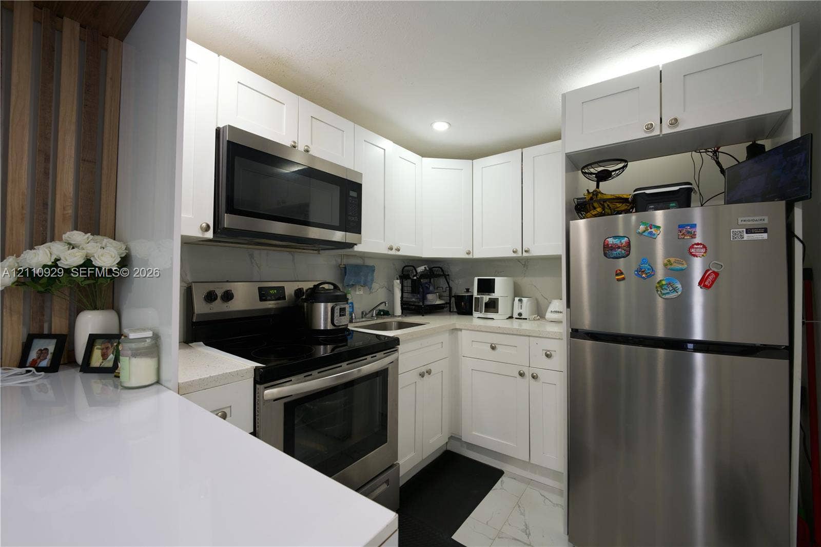 Kitchen featuring white Shaker-style cabinetry, stainless steel appliances, white stone-composite countertops, and a full-height stone-finish backsplash