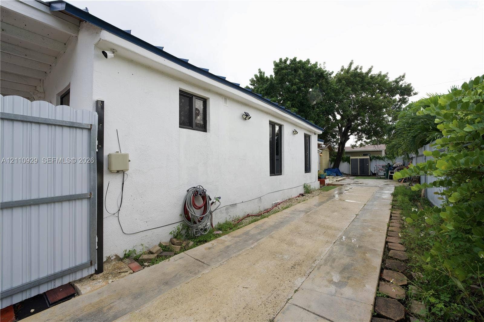 Stucco exterior finish with inset windows, white metal side gate, and concrete paved pathway