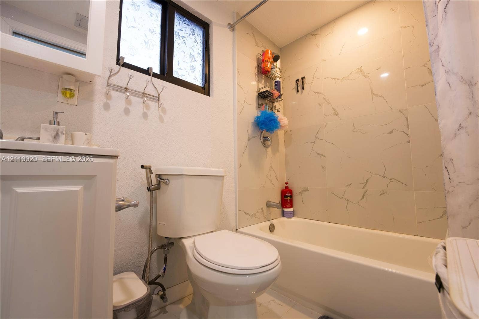 Full bathroom featuring a white vanity cabinet, a tub-shower combination with light-toned wall tile, a window, and chrome hardware