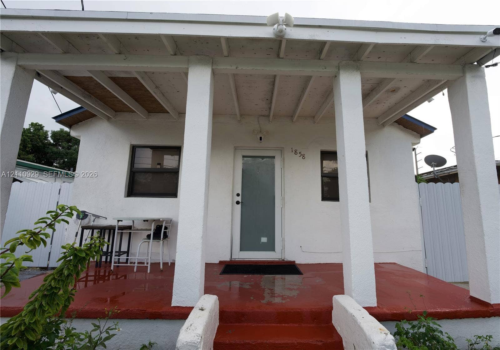 Covered front porch featuring structural columns, a painted concrete floor, exposed wood ceiling rafters, and an exterior door with a frosted glass panel