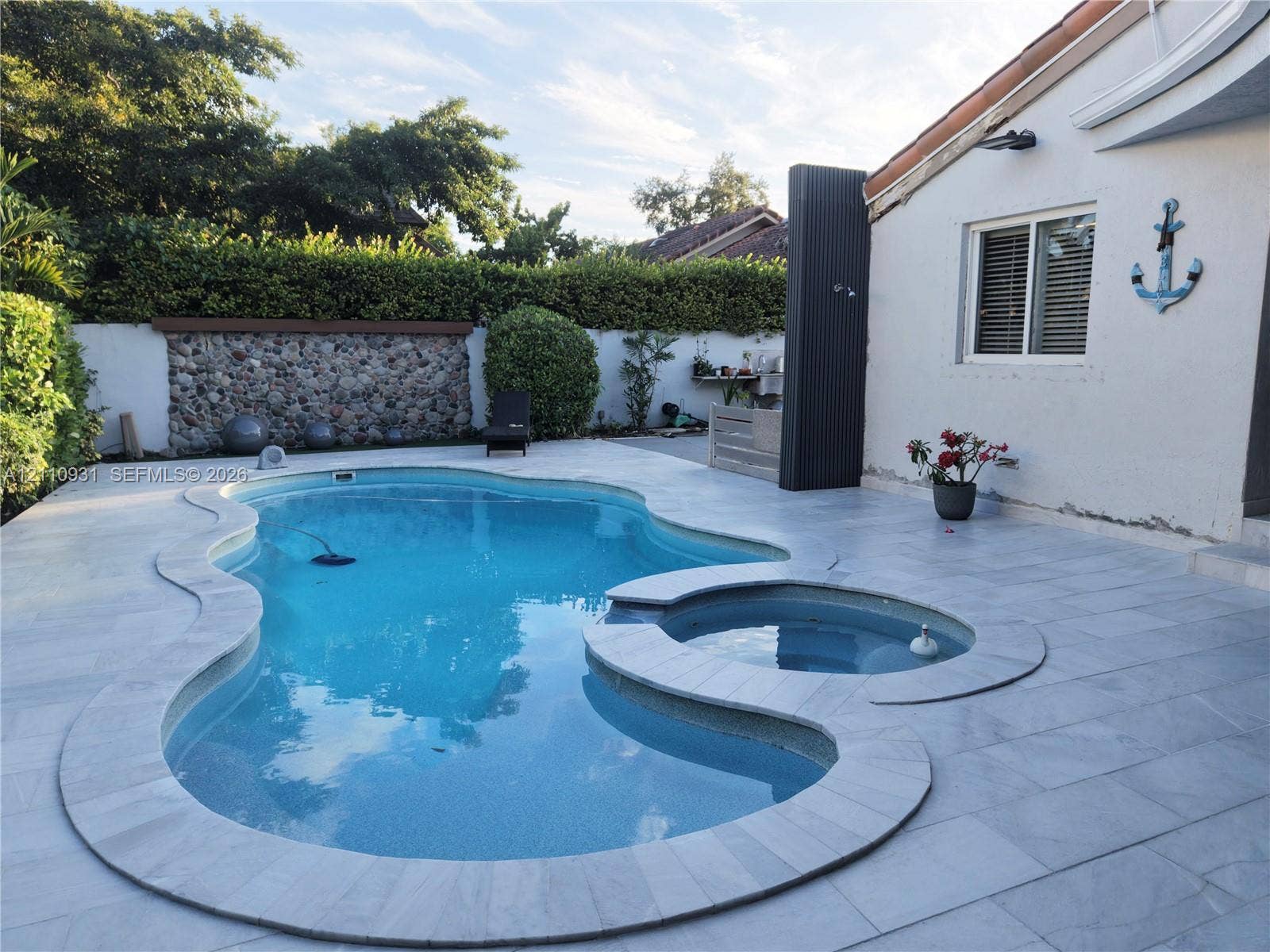 3005 SW 99th Court, Miami, FL 33165 Inground swimming pool with attached circular spa, surrounded by stone-tile decking and bordered by a decorative stone-accent wall