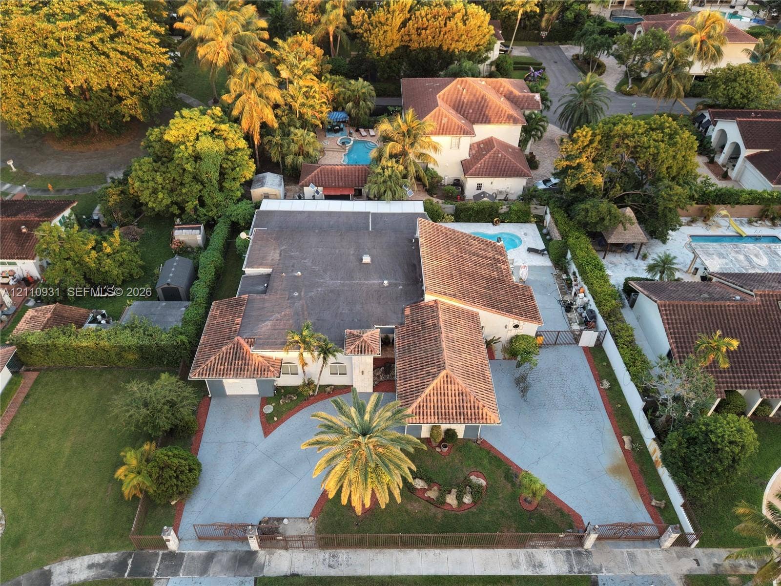 3005 SW 99th Court, Miami, FL 33165 Single-story residence featuring a clay tile roof, expansive paved driveway, swimming pool, and mature perimeter landscaping