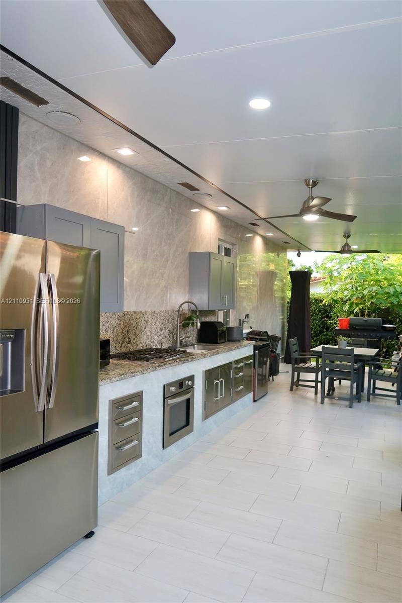 3005 SW 99th Court, Miami, FL 33165 Outdoor kitchen featuring stone countertops, built-in stainless steel appliances, cabinetry with light gray finish, recessed ceiling lighting, and large-format tile flooring