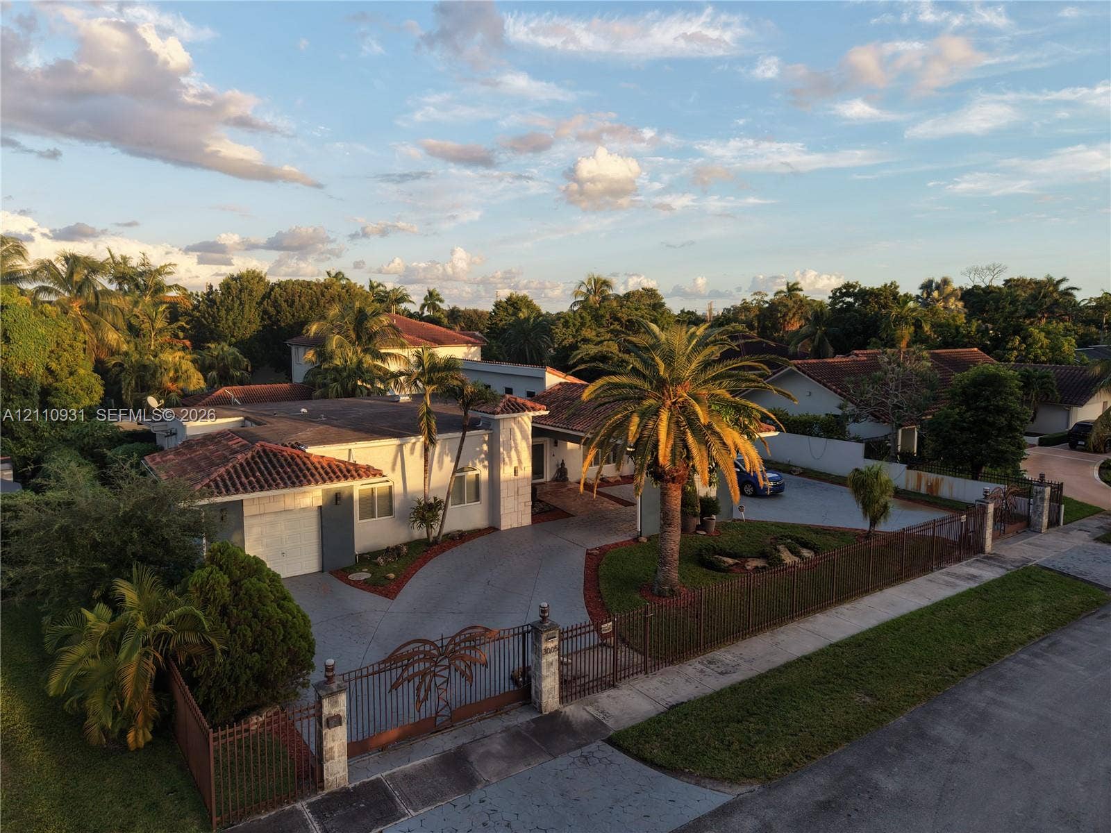 3005 SW 99th Court, Miami, FL 33165 Single-story residence featuring a tile roof, gated concrete driveway, metal perimeter fencing, and mature palm landscaping