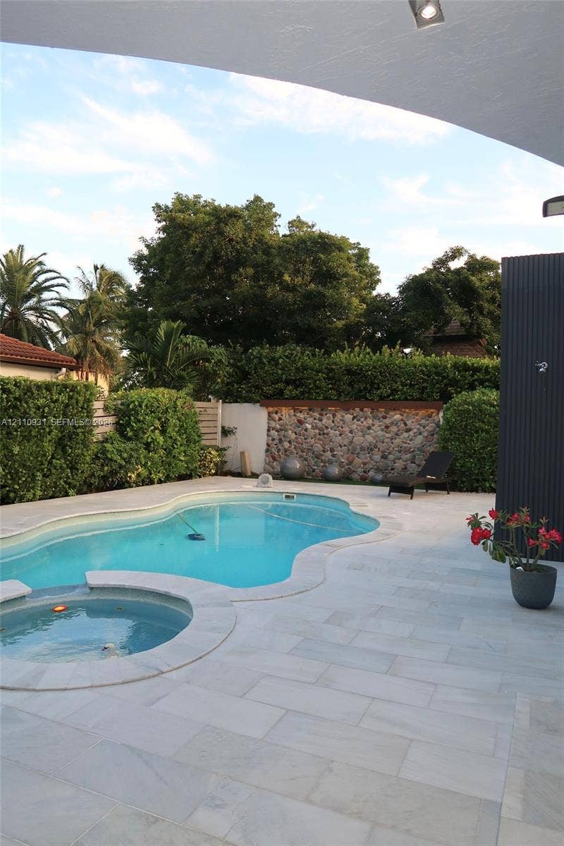 3005 SW 99th Court, Miami, FL 33165 Free-form swimming pool with integrated spa, stone-accented perimeter wall, and light-toned paved decking