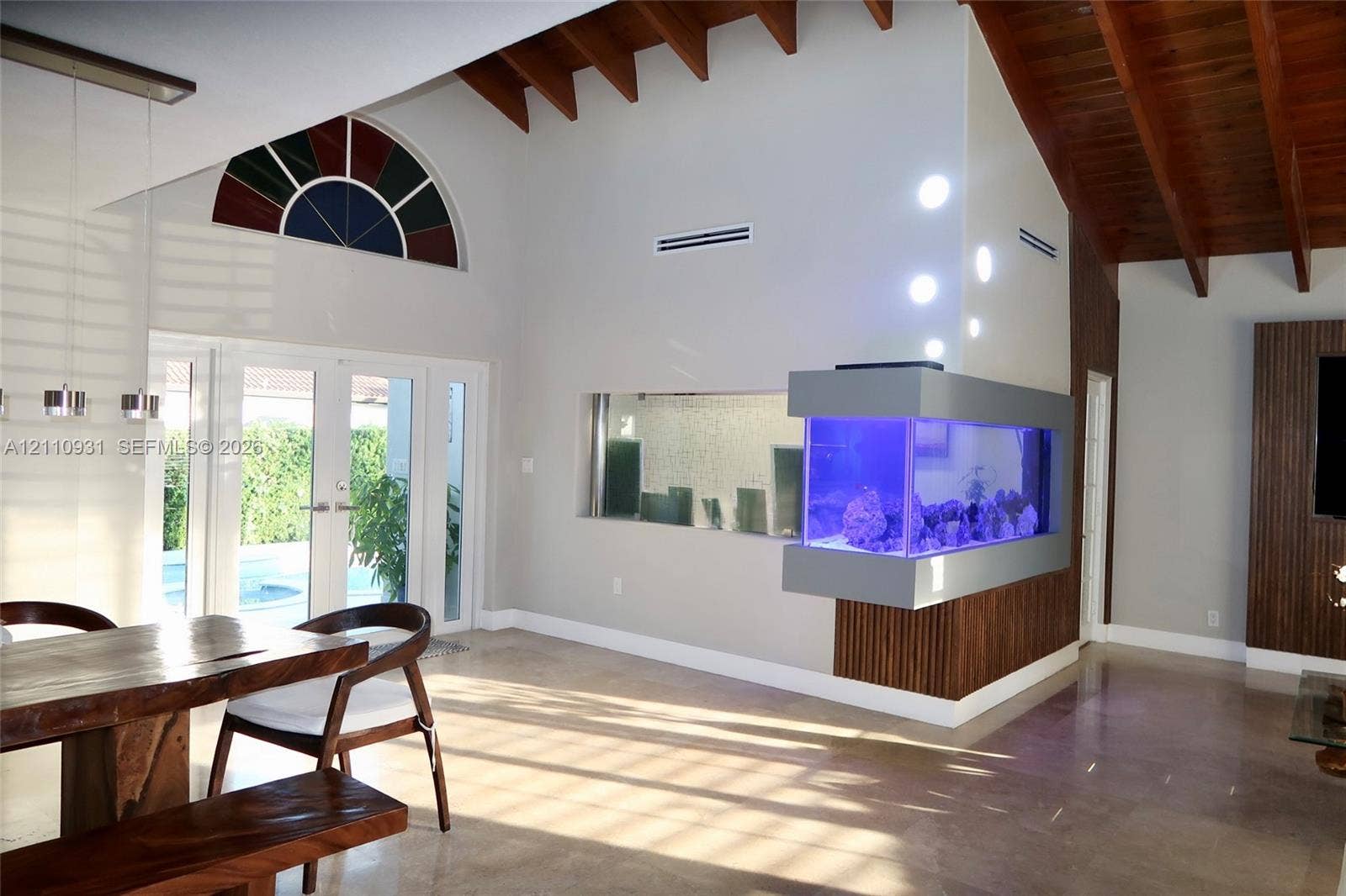 3005 SW 99th Court, Miami, FL 33165 Vaulted ceiling featuring exposed wood beams, built-in recessed aquarium, arched accent window, glass-paneled double doors, and polished stone flooring