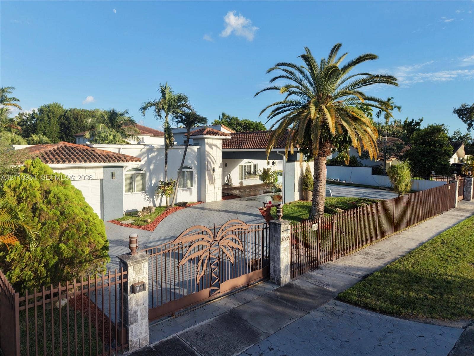 3005 SW 99th Court, Miami, FL 33165 Single-story residence featuring a tile roof, decorative metal security gate, paved driveway, masonry perimeter fencing, and mature landscaping