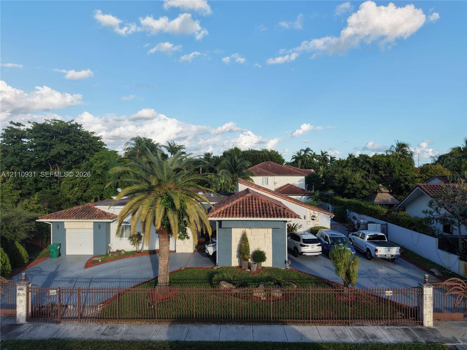 3005 SW 99th Court, Miami, FL 33165 Single-story residence featuring a Mediterranean-inspired tile roof, masonry facade accents, an attached two-car garage, expansive concrete driveway, and a perimeter metal fence