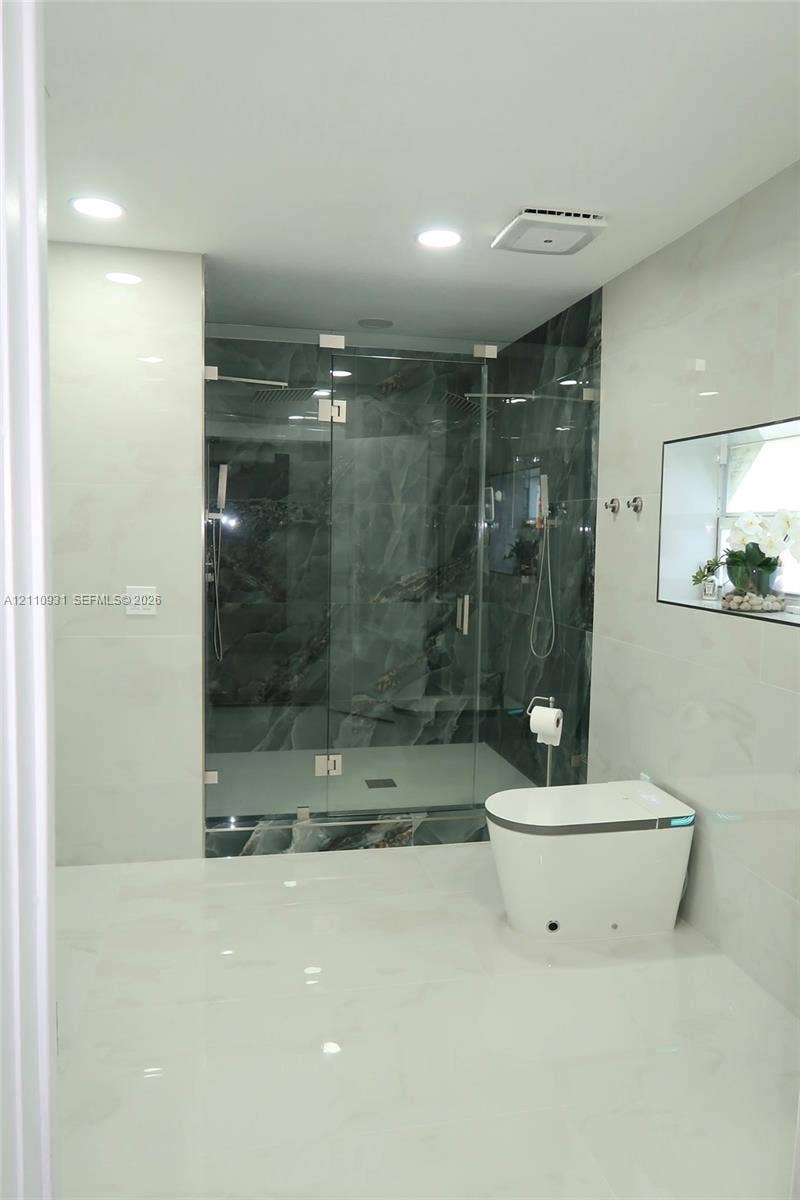 3005 SW 99th Court, Miami, FL 33165 Walk-in glass-enclosed shower with dark stone-patterned tile, white floor-to-ceiling wall tile, recessed lighting, and a modern low-profile toilet