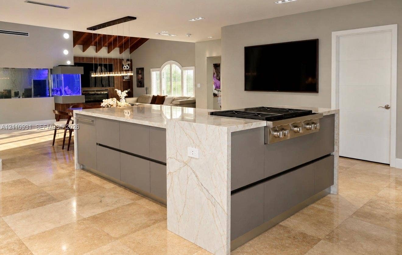 3005 SW 99th Court, Miami, FL 33165 Kitchen island featuring a waterfall stone countertop, integrated gas cooktop, matte-finish cabinetry, and polished tile flooring