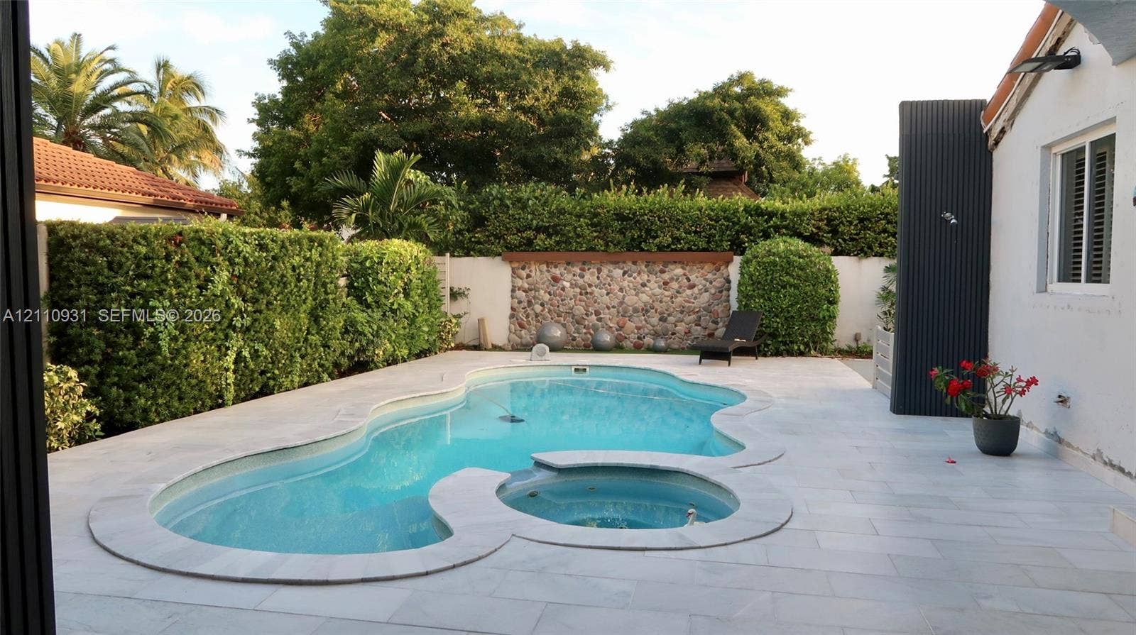 3005 SW 99th Court, Miami, FL 33165 Freeform swimming pool and integrated spa, light-toned stone decking, and decorative stone masonry feature wall surrounded by privacy hedging