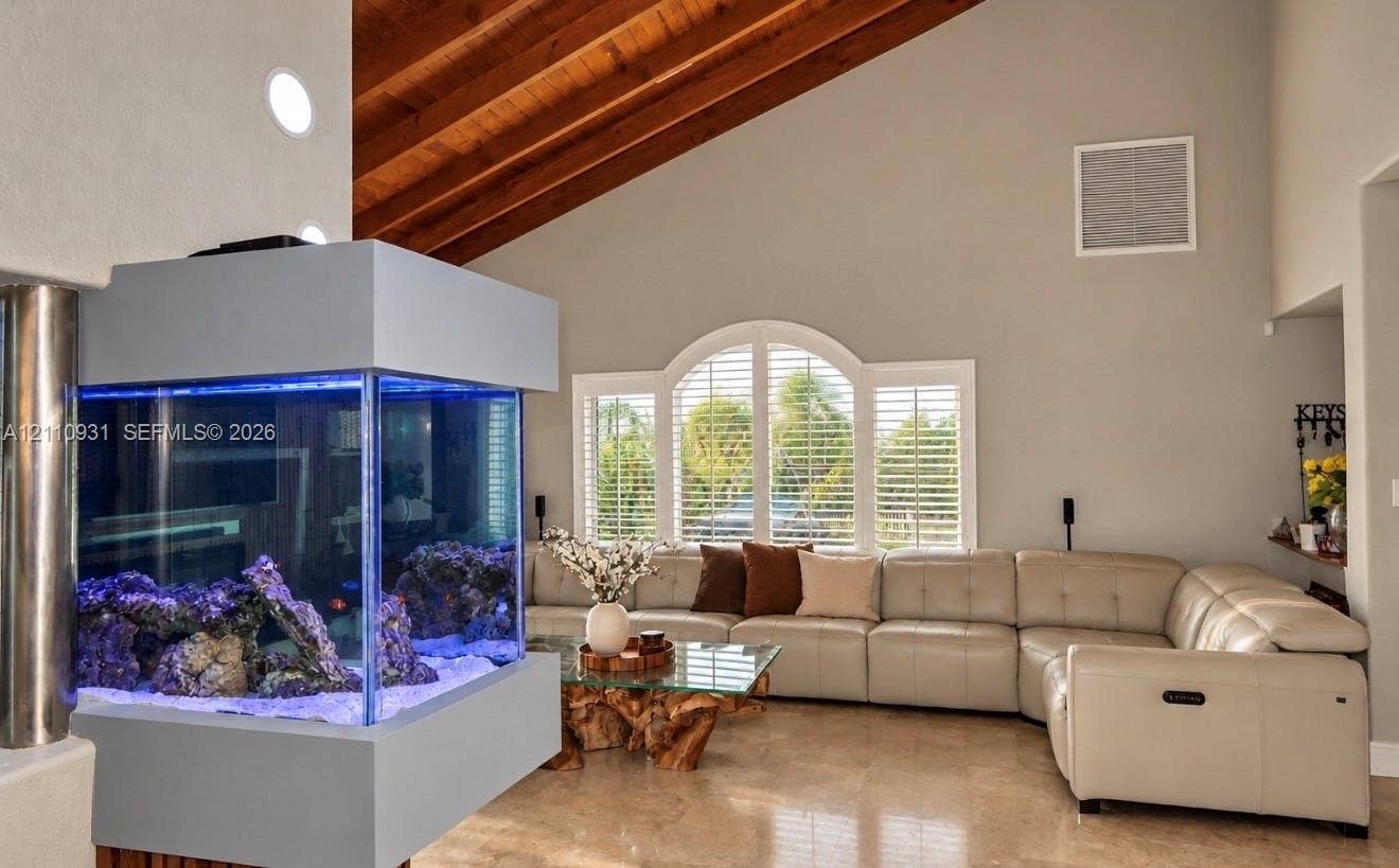 3005 SW 99th Court, Miami, FL 33165 Vaulted ceilings featuring exposed wood beams, built-in structural aquarium, arched window with integrated plantation shutters, and polished stone flooring