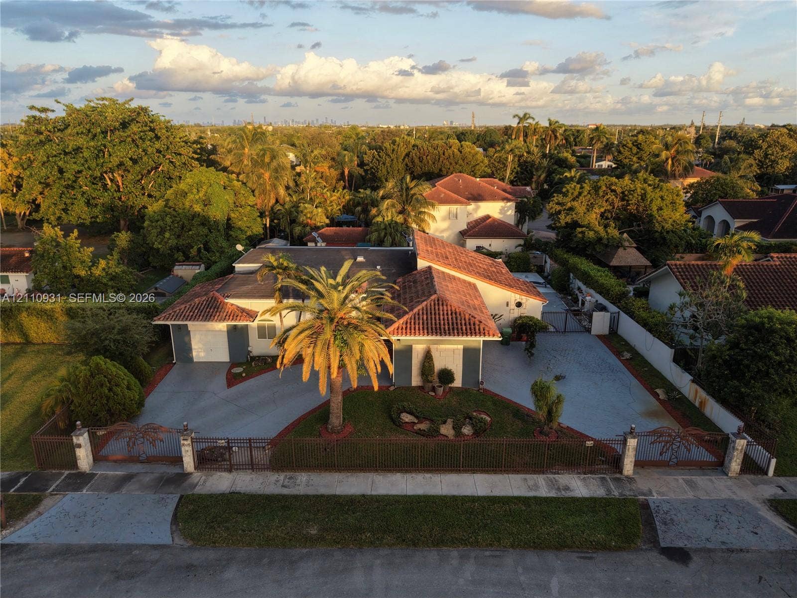 3005 SW 99th Court, Miami, FL 33165 Single-story residence featuring a terracotta-tiled roof, an expansive paved driveway, and decorative metal perimeter fencing