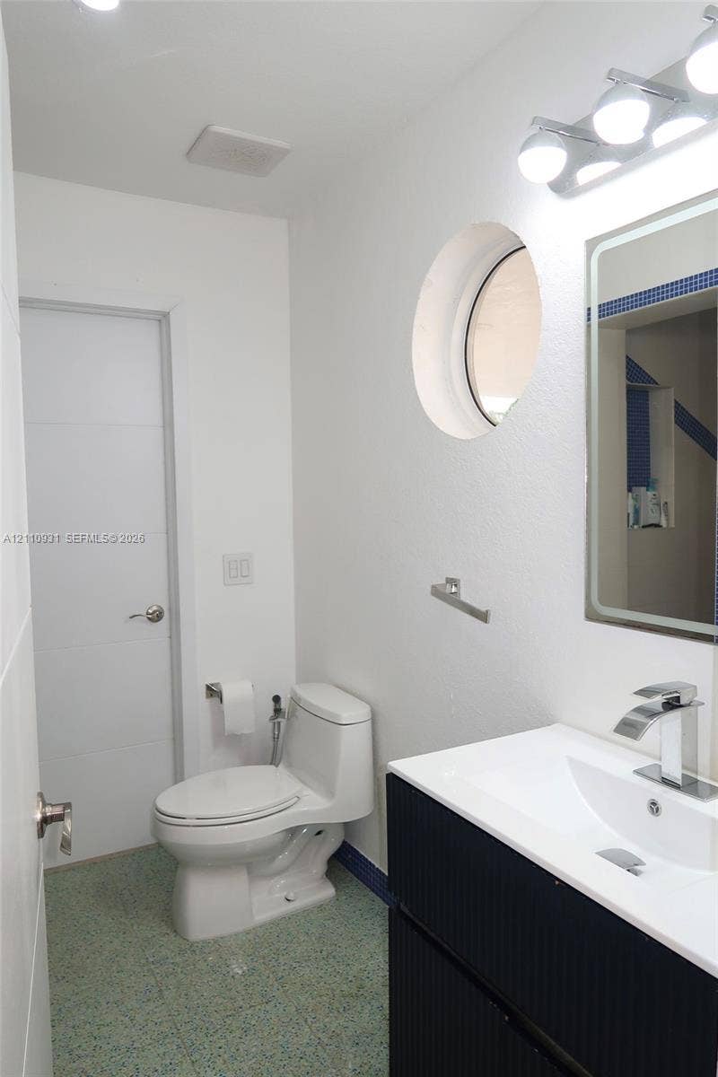 3005 SW 99th Court, Miami, FL 33165 Bathroom featuring a black vanity with a white countertop and integrated sink, chrome-finish faucet, circular accent window, and wall-mounted vanity light fixture