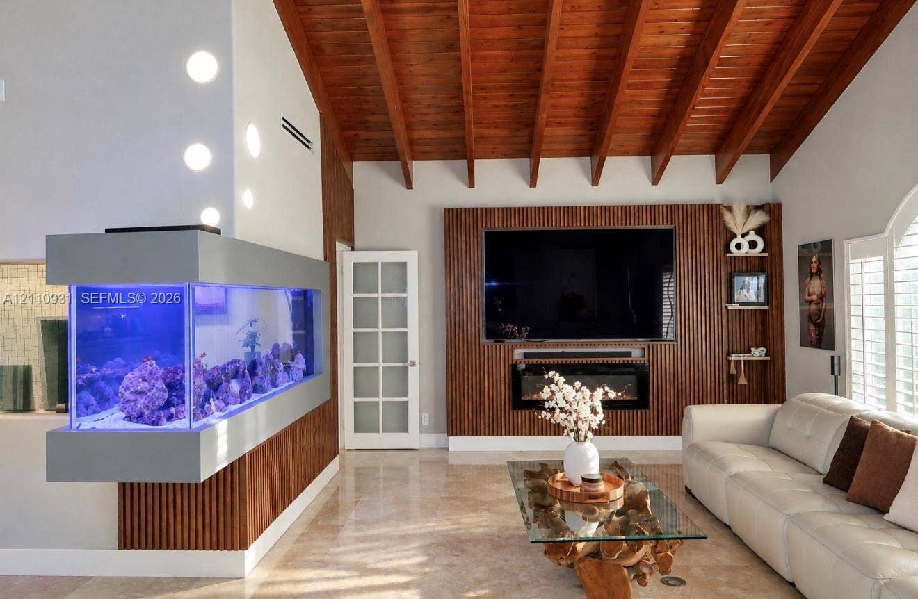 3005 SW 99th Court, Miami, FL 33165 Vaulted wood-plank ceiling with exposed rafters, custom floor-to-ceiling slatted wood wall paneling, built-in electric fireplace, wall-mounted aquarium, and polished stone flooring