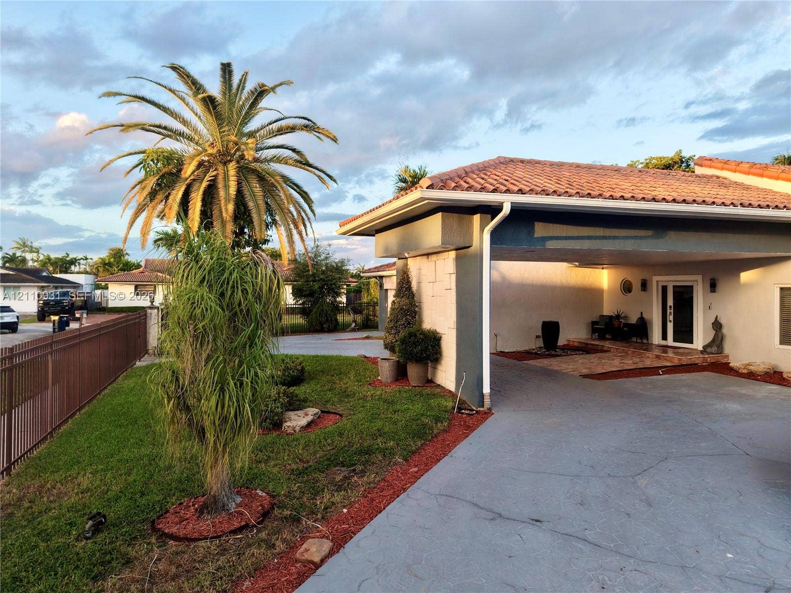 3005 SW 99th Court, Miami, FL 33165 Exterior facade featuring a terracotta-tiled roof, covered entryway, textured masonry detailing, concrete driveway, and mature palm landscaping