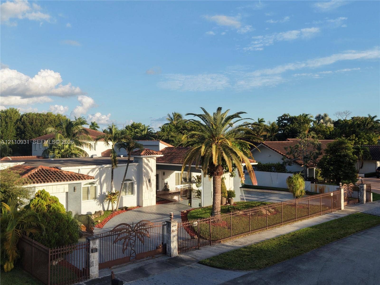 3005 SW 99th Court, Miami, FL 33165 Single-story residence featuring a terracotta tile roof, decorative metal perimeter fencing, paved driveway, and mature palm tree landscaping