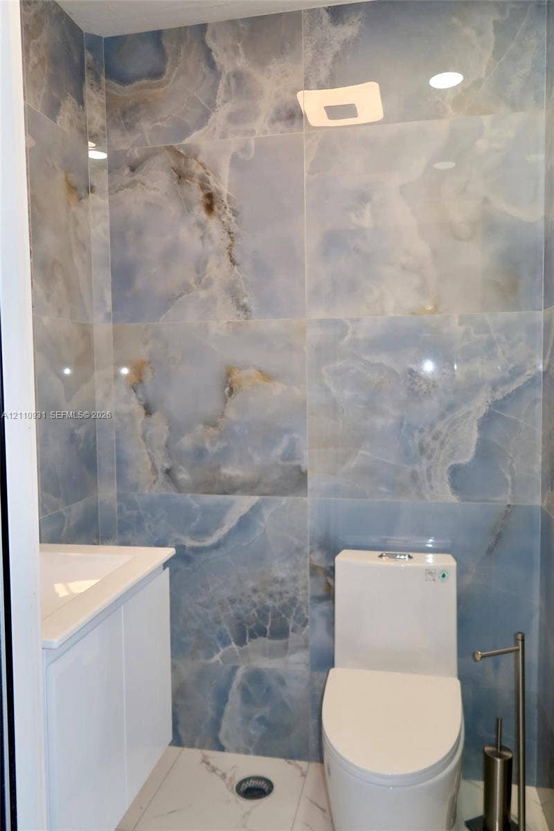 3005 SW 99th Court, Miami, FL 33165 Full-height polished stone wall tile with blue veining, white vanity with integrated sink, and dual-flush toilet