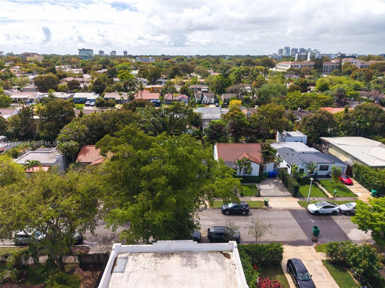 Aerial perspective of a surrounding residential neighborhood characterized by dense tree canopy, paved streets, and a diverse collection of single-story structures