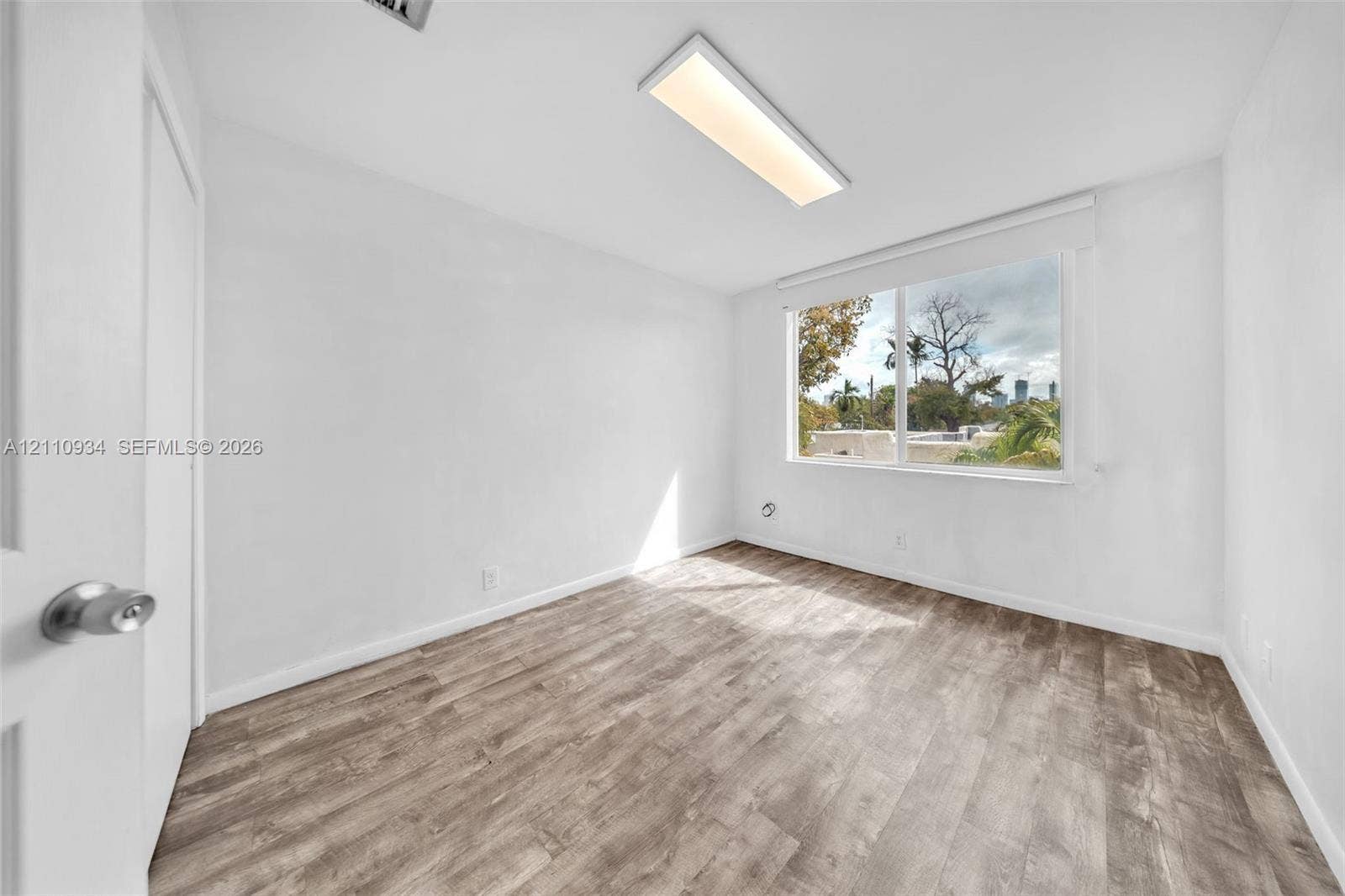 Interior room featuring wood-finish flooring, a large window, and a rectangular ceiling-mounted light fixture