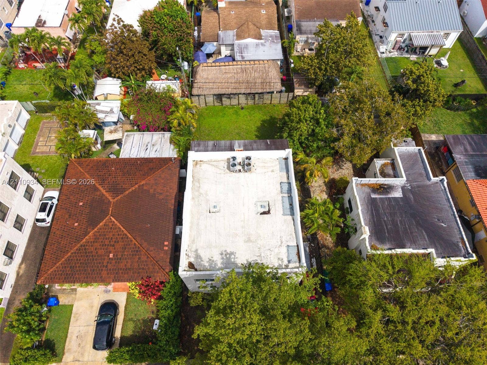Aerial perspective of a detached residential property featuring a flat roof with mounted HVAC units, mature landscaping, and an expansive grass lawn