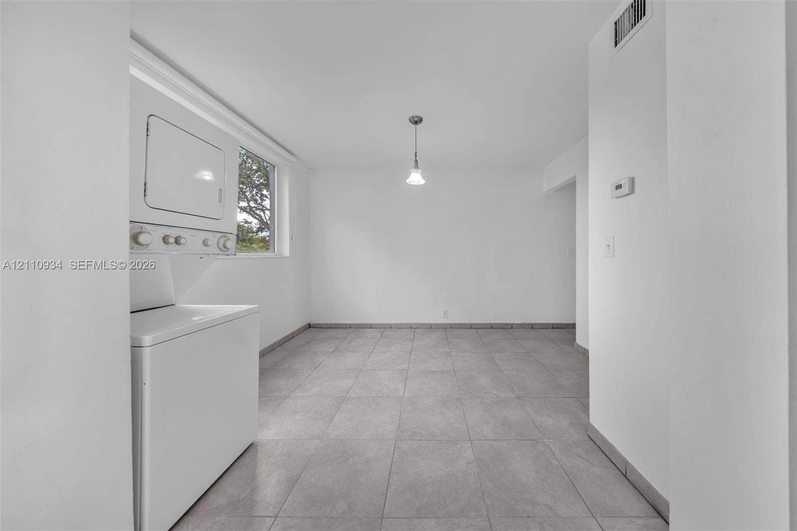 Neutral-toned tile flooring, stacked laundry unit, single-pendant ceiling fixture, and large rectangular window