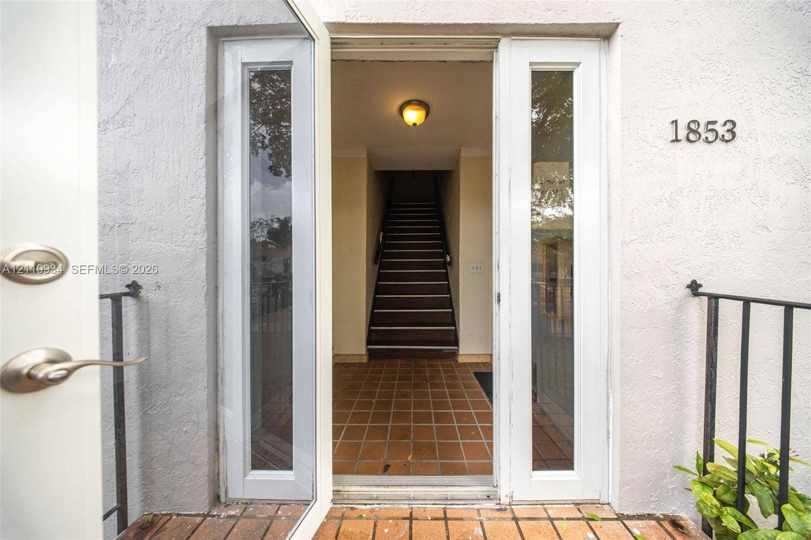 Entryway featuring double glass-paneled doors, terracotta tile flooring, a flush-mount ceiling light fixture, and a black metal handrail