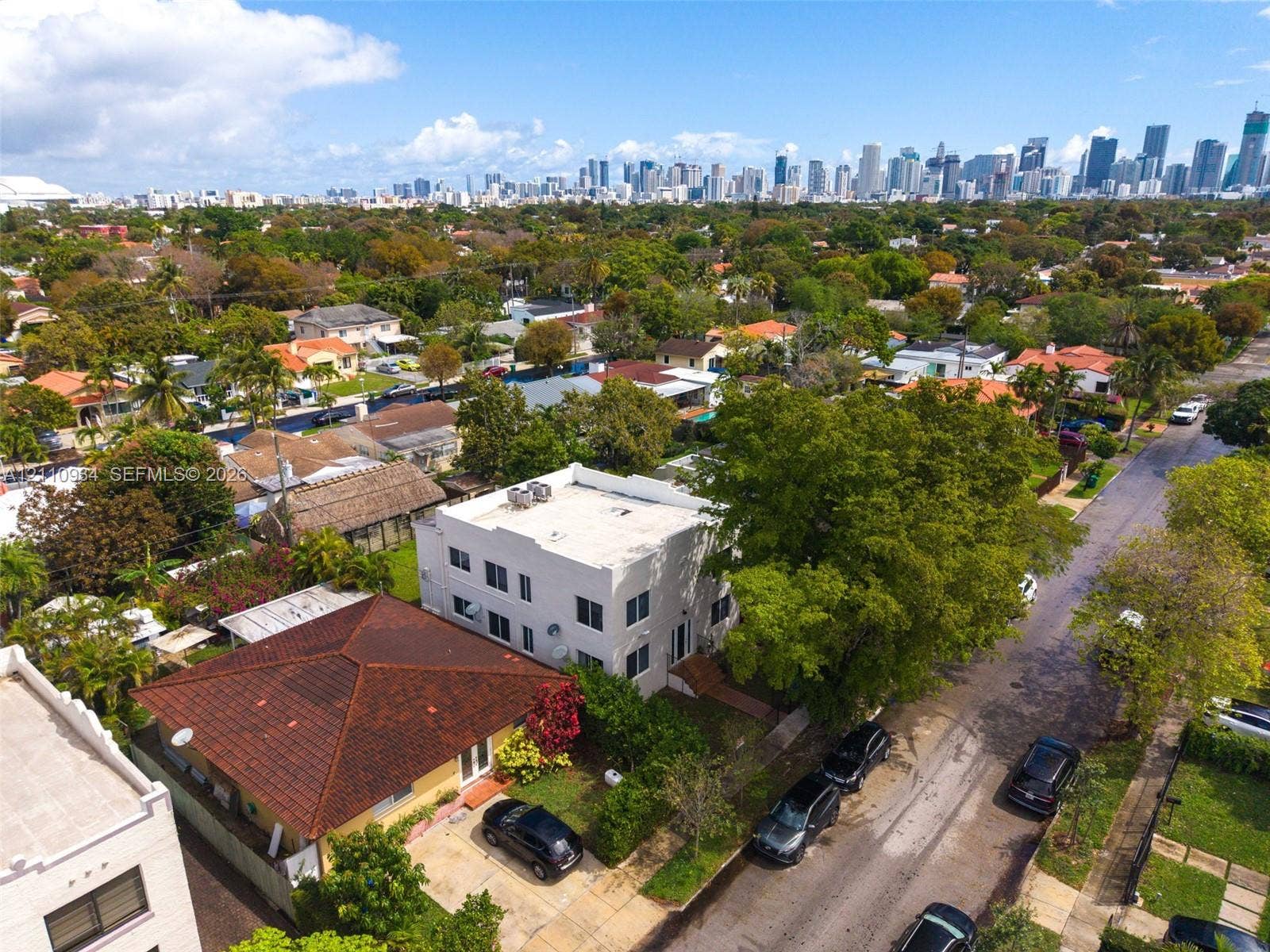 Aerial perspective of a multi-level structure featuring a flat roof, white exterior cladding, and urban skyline backdrop