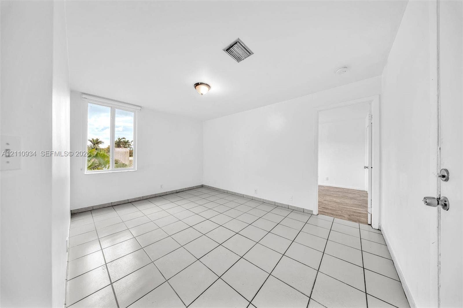 Neutral-toned square tile flooring, white wall finishes, single-pane window, and flush-mount ceiling light fixture