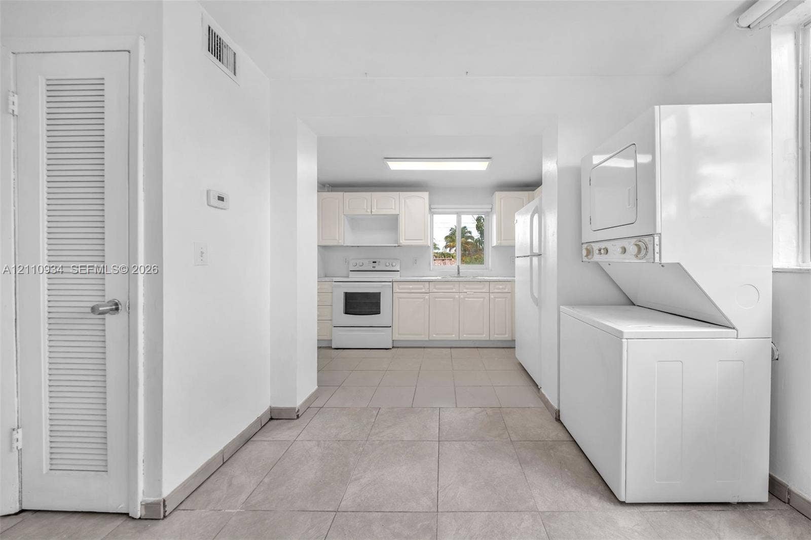 Kitchen featuring light-toned cabinetry, white appliances, and ceramic tile flooring, with a dedicated laundry area including a stacked washer and dryer