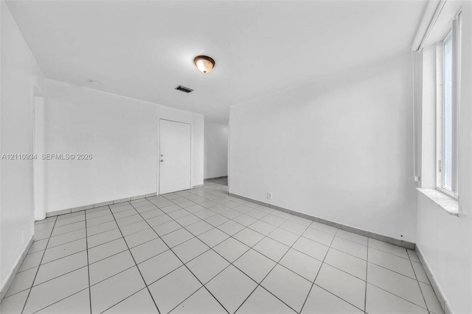 Interior space featuring large-format ceramic tile flooring, neutral white walls, and a recessed window with a stone-finish sill