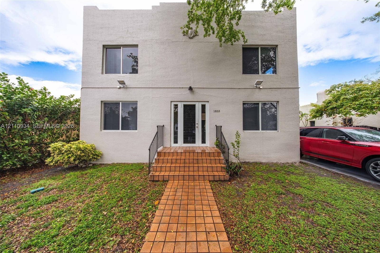 Two-story exterior featuring a stucco facade, stepped roofline, tiled front steps, tiled walkway, and full-light front entry door with sidelights