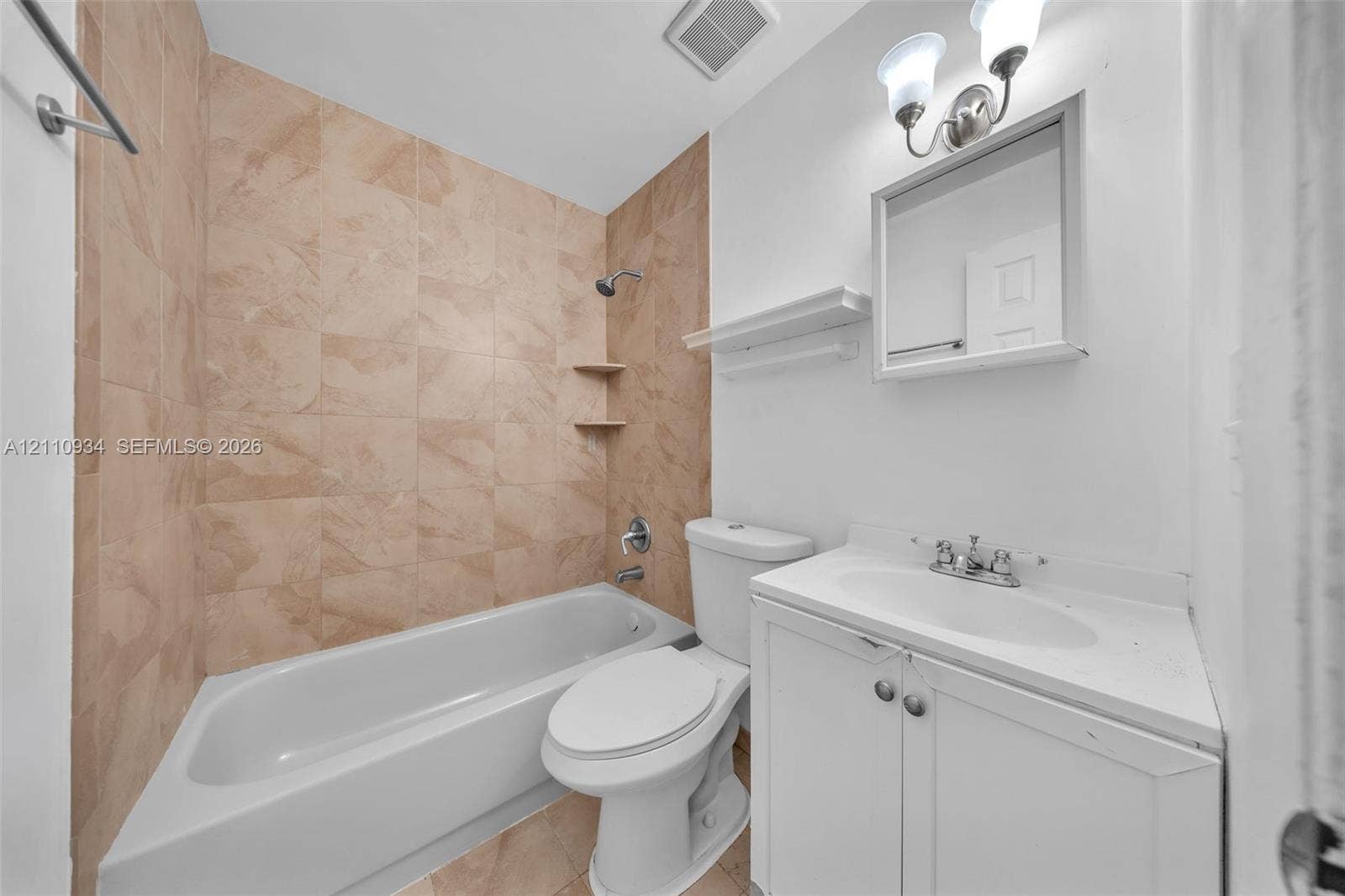 Full bathroom featuring a tub-shower combination with tiled surround, integrated shelving, white vanity with an inset sink, and a dual-light wall-mounted fixture