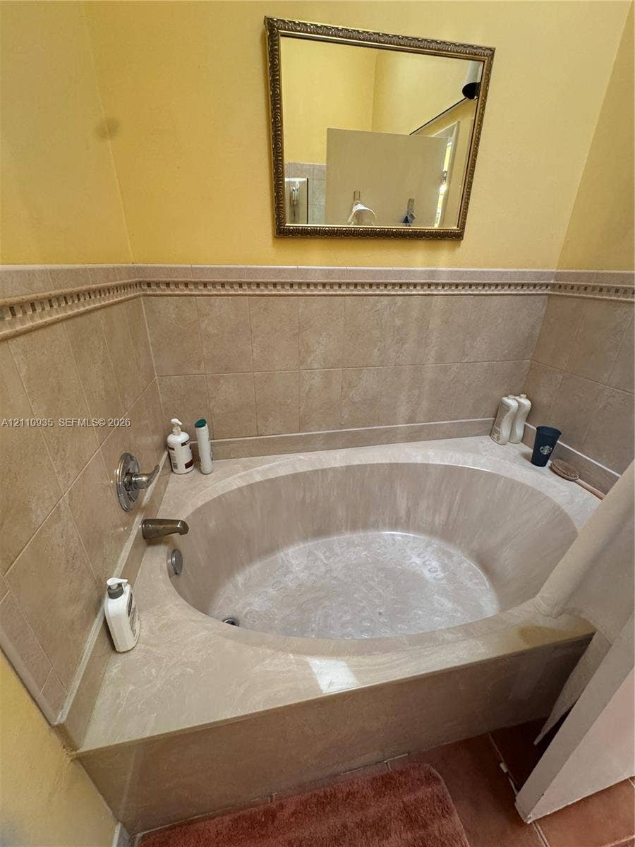 3530 Magellan Circle, #618, Aventura, FL 33180 Oval soaking tub with a tiled surround, decorative chair rail tile accent, and wall-mounted metallic fixtures, complemented by a rectangular wall-mounted mirror