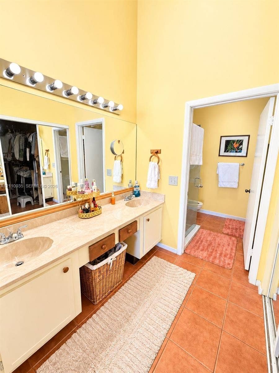 3530 Magellan Circle, #618, Aventura, FL 33180 Dual-sink vanity with solid-surface countertop, full-width wall-mounted mirror, tiered vanity lighting, and ceramic tile flooring