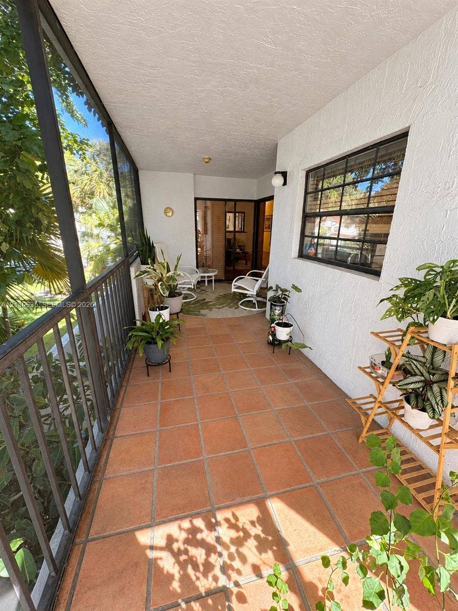 3530 Magellan Circle, #618, Aventura, FL 33180 Screened-in porch featuring terracotta tile flooring, textured stucco walls, and black-framed metal railings