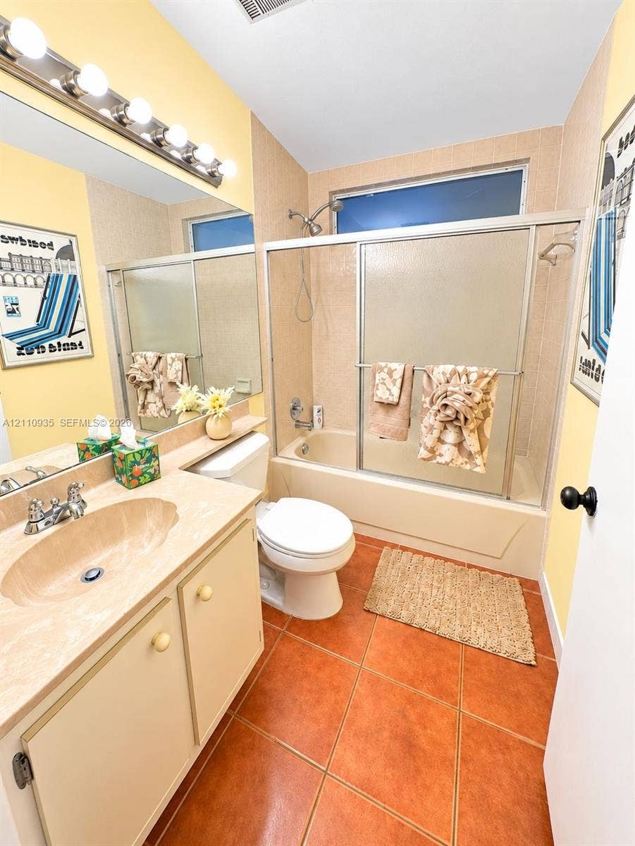 3530 Magellan Circle, #618, Aventura, FL 33180 Bathroom featuring terracotta-style tile flooring, vanity with integrated sink, full-width wall mirror, and tub-shower combination with sliding glass doors