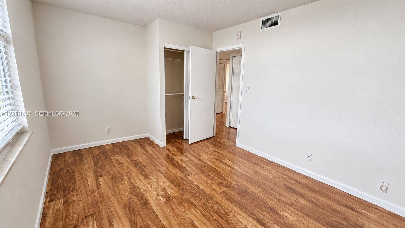 Room featuring wood-finish flooring, neutral wall paint, and a built-in closet with an interior shelf and rod