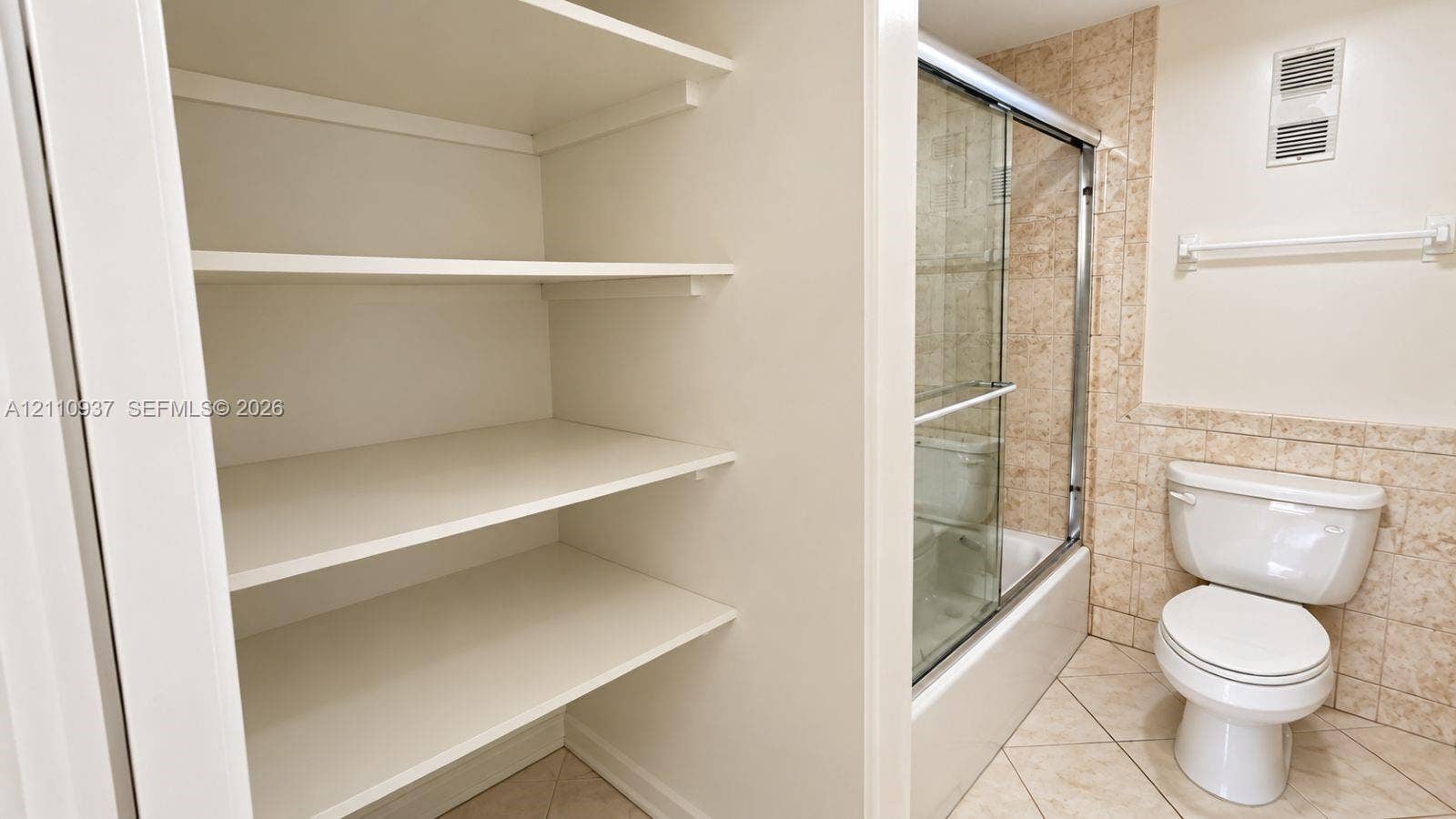 Built-in storage shelving, walk-in shower with a sliding glass door, ceramic tile surround, and tile flooring