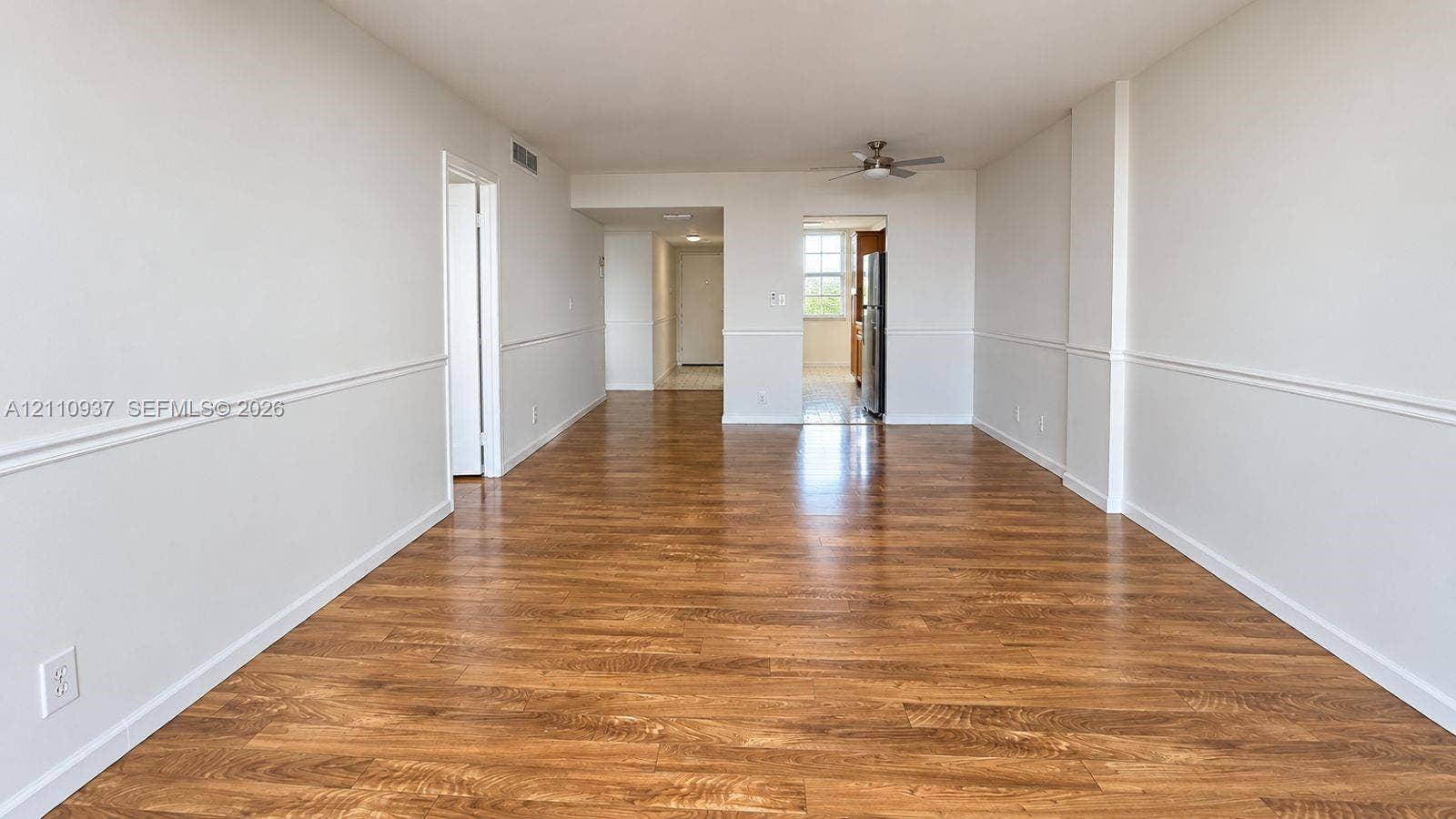Open-concept interior featuring wood-finish flooring, chair rail molding, and a ceiling-mounted fan