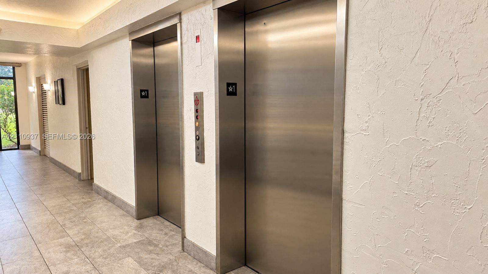 Dual stainless steel elevators featuring brushed metal finishes and textured wall surfaces with neutral floor tiling
