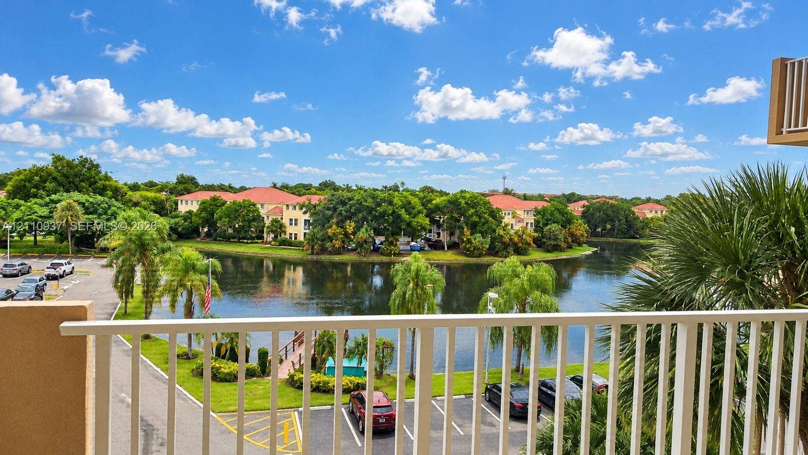 Balcony featuring white metal railings, overlooking a lake with mature palms and landscaped grounds