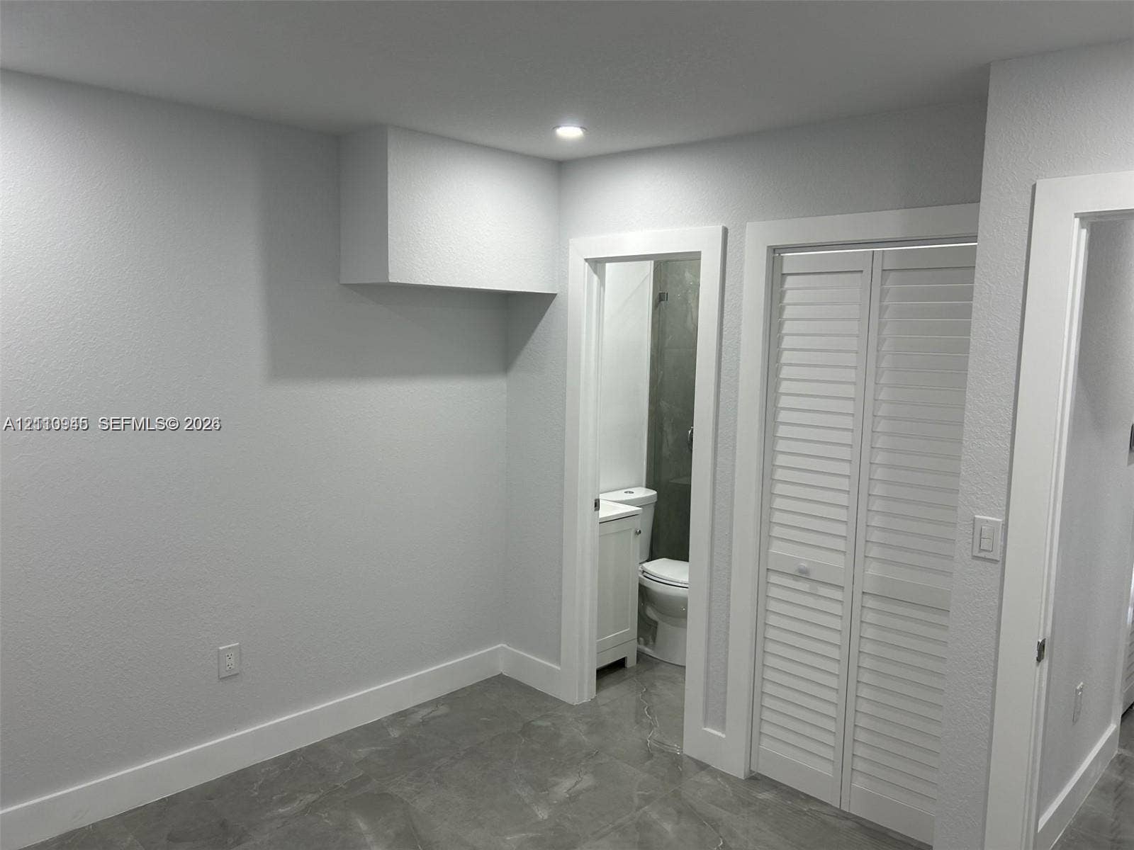 Neutral-toned interior space featuring light grey ceramic tile flooring, recessed ceiling lighting, and white louvered closet doors