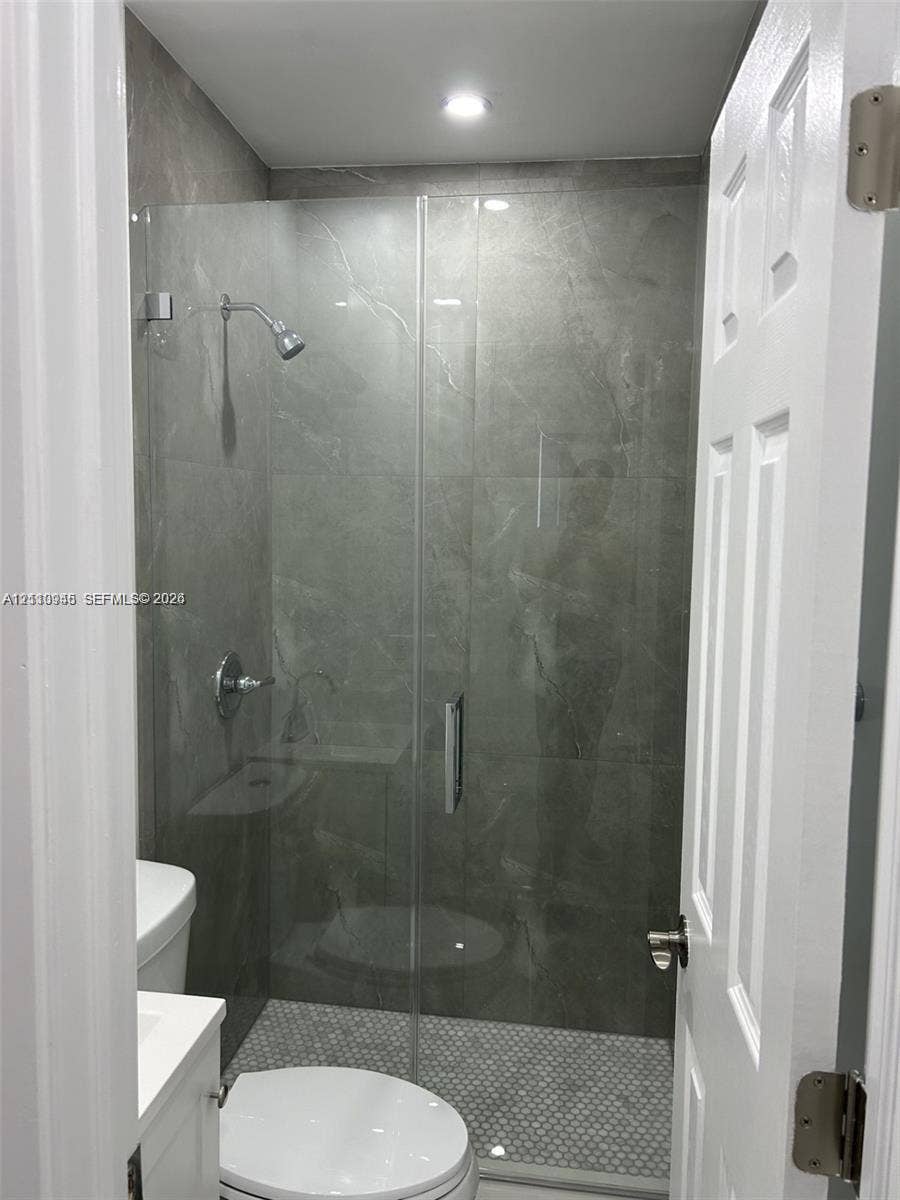 Walk-in shower featuring large-format stone-finish tile surround, frameless glass enclosure, recessed ceiling lighting, and mosaic tile shower floor