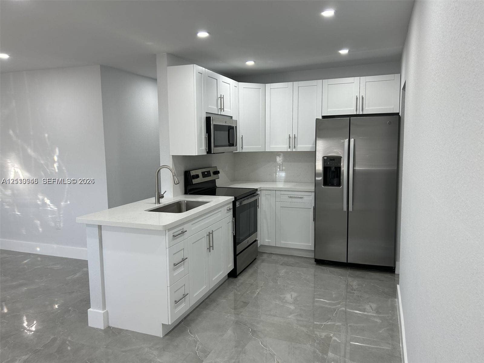 Kitchen featuring white cabinetry, solid-surface countertops, stainless steel appliances, a undermount sink with a gooseneck faucet, and stone-finish flooring