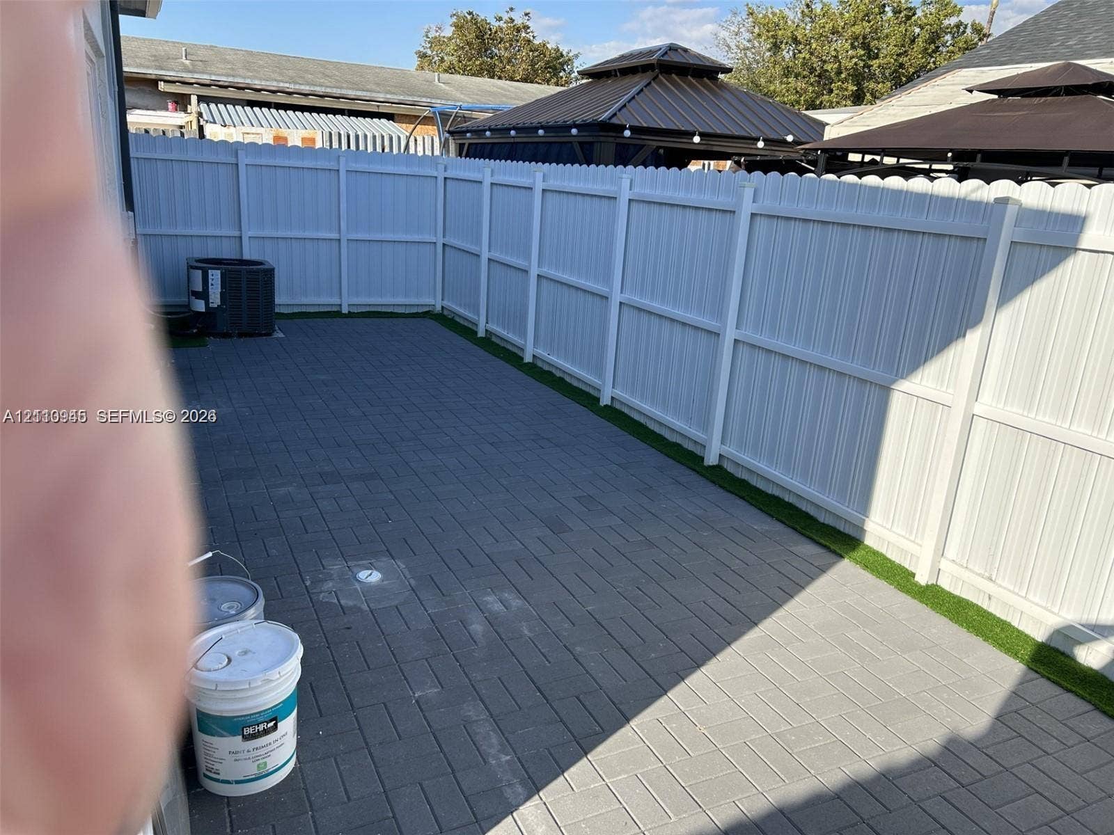 Enclosed outdoor space featuring a charcoal-toned paver patio, synthetic turf border, and white vinyl privacy fencing