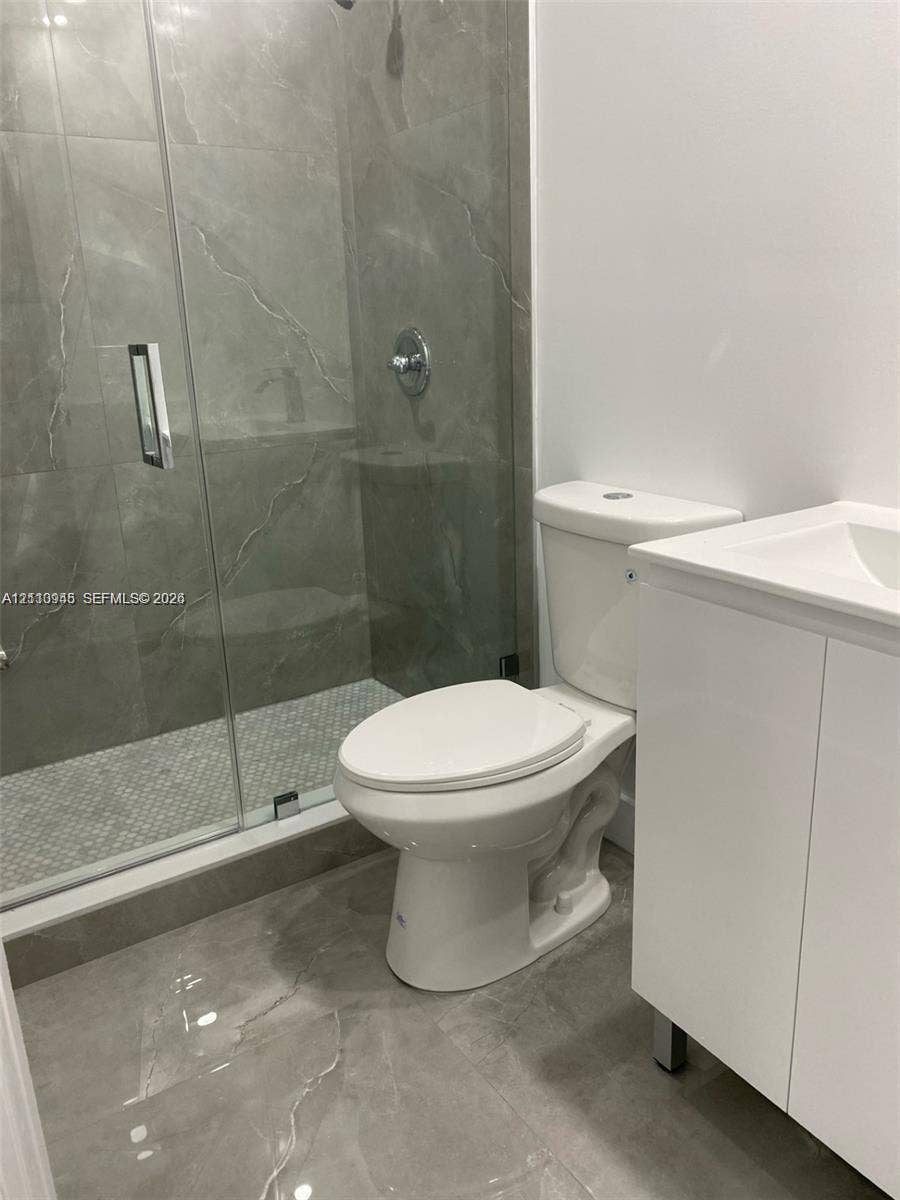 Walk-in shower with large-format tile surround, glass enclosure, mosaic tile floor, white vanity cabinet, and modern polished chrome fixtures